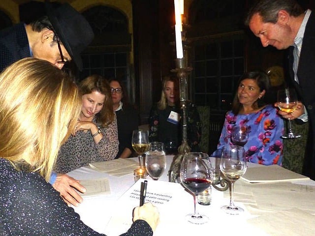 Mister Vibe analyzing the handwriting of a group seated at a table.