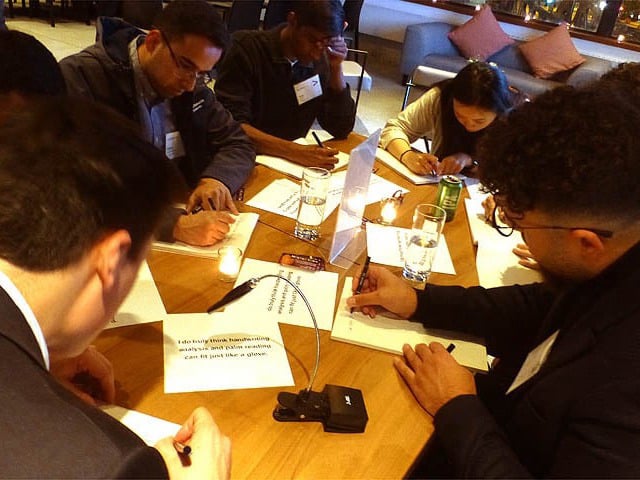 People seated at table writing handwriting samples.