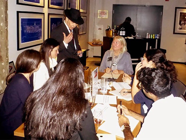 Mister Vibe analyzing the handwriting of a group seated at a table.