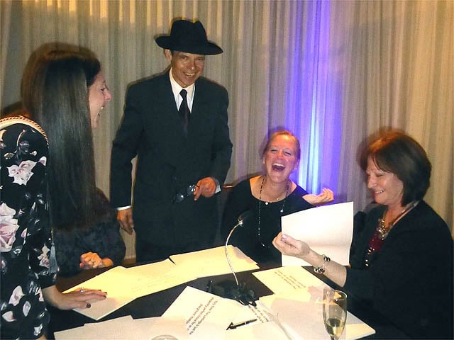 Three women laugh as Mister Vibe analyzes their handwriting at a trade show.